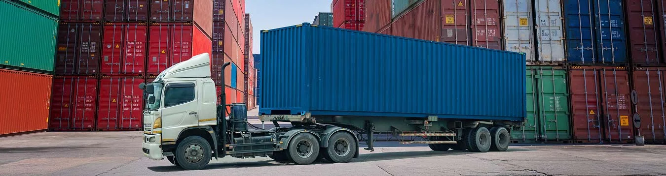 Container truck at port terminal between stacked shipping containers